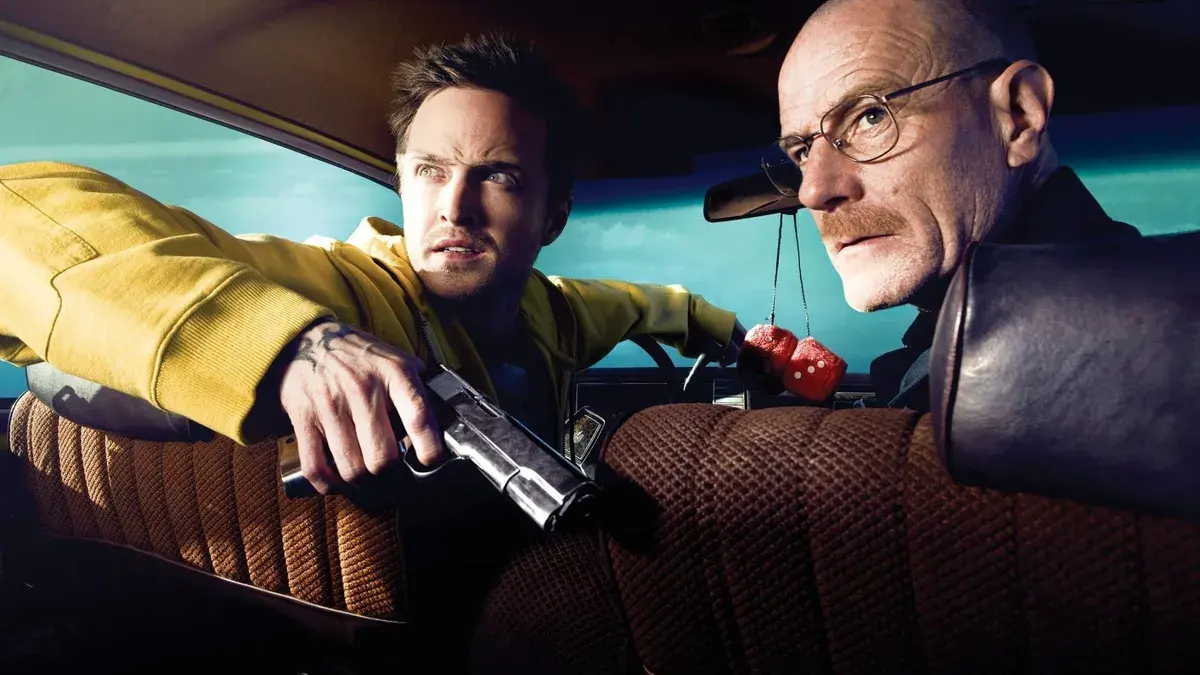 Breaking Bad : Aaron Paul en Jesse Pinkman, pistolet à la main, penché vers Bryan Cranston en Walter White dans une voiture