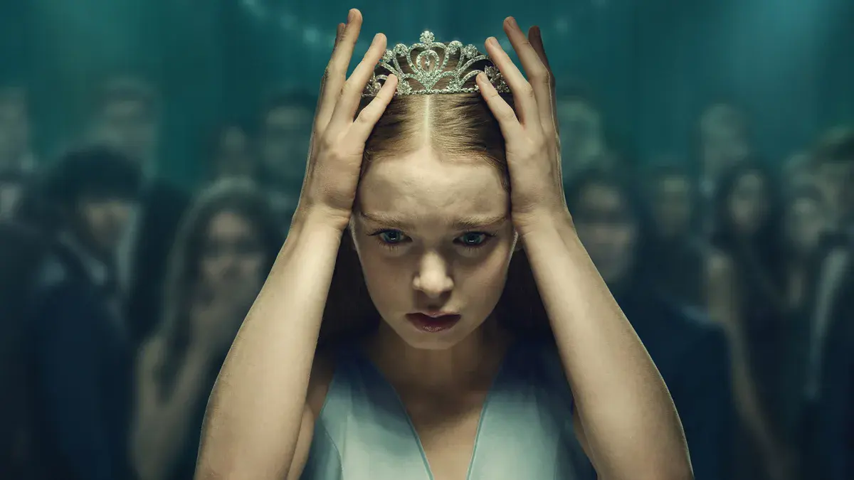 Carrie White (Summer H. Howell), une tiare sur la tête, se tient le crâne à deux mains devant la foule du bal dans la série Carrie