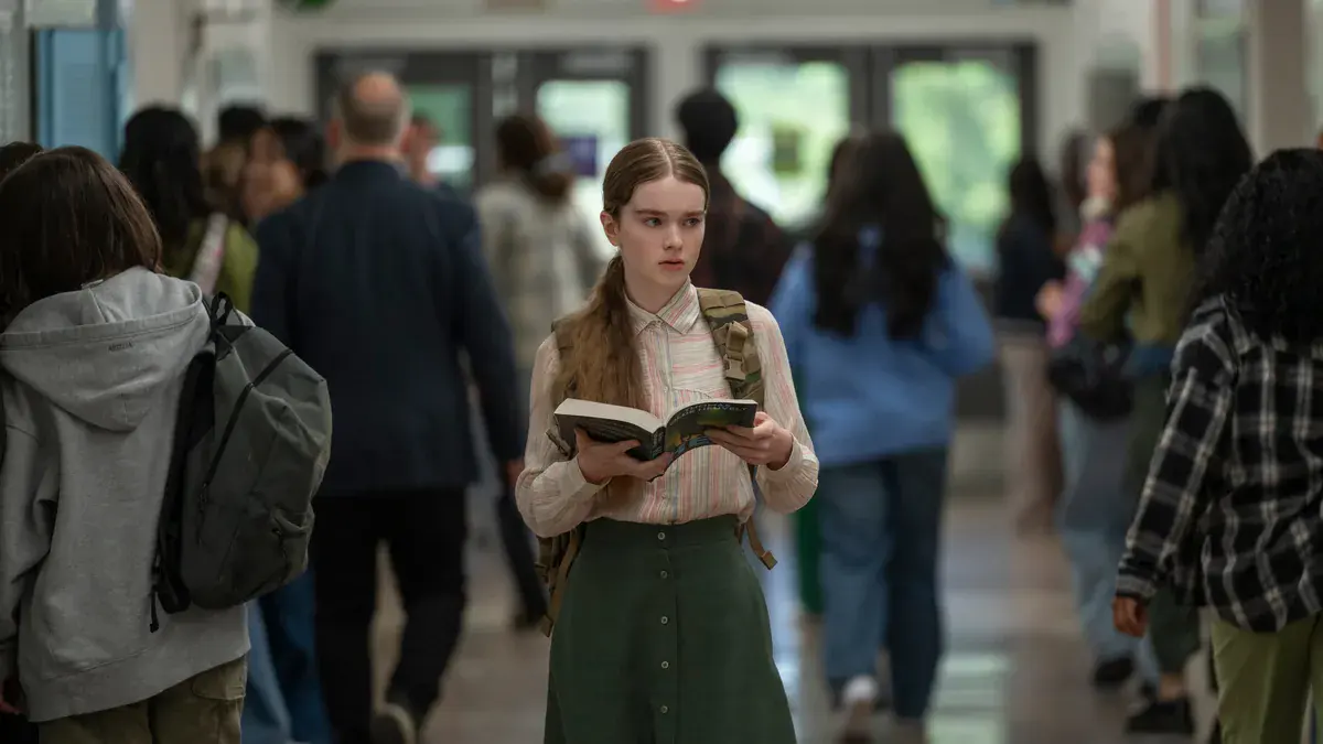 Summer H. Howell en Carrie White, un livre ouvert à la main, traverse un couloir de lycée bondé dans la série Carrie de Prime Video