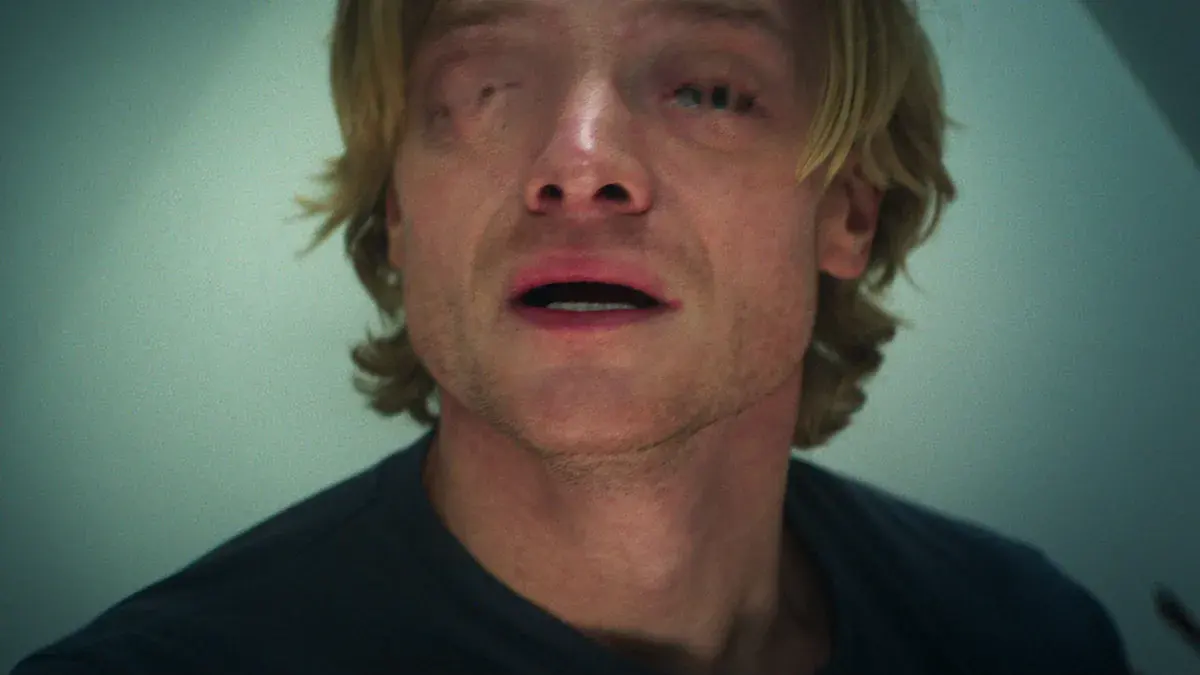 Gros plan de Tom Rhys Harries en Matt Hagen, le visage abîmé et la bouche entrouverte, sous une lumière blafarde, dans Clayface