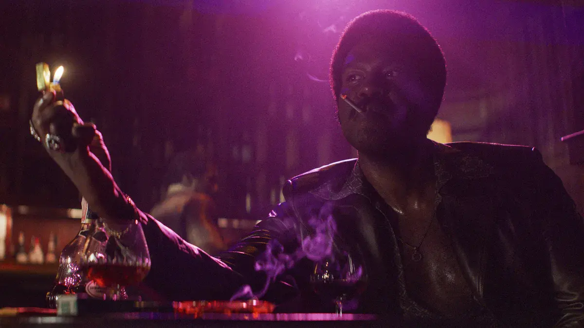 Yahya Abdul-Mateen II en Roderick « Hot Rod » Harrison, cigarette aux lèvres sous une lumière violette, dans The Further Mis-Adventures of Cliff Booth