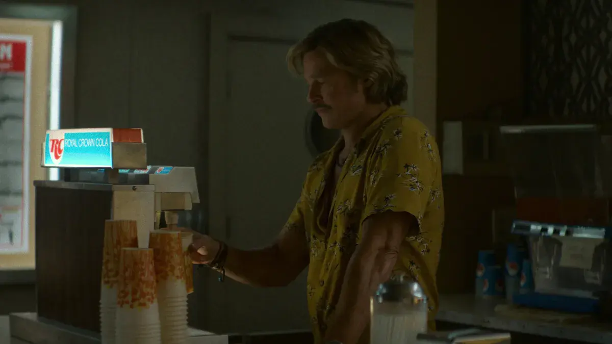 Brad Pitt en Cliff Booth derrière le comptoir de RC Cola du New Beverly Cinema dans The Further Mis-Adventures of Cliff Booth