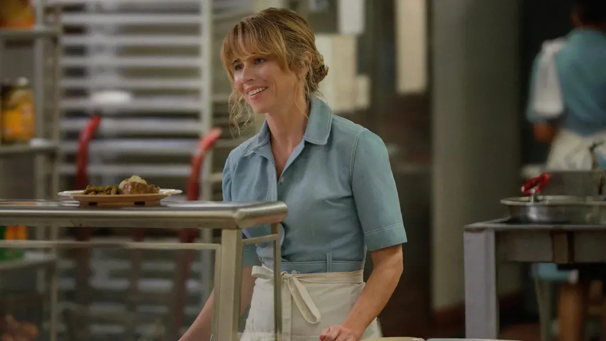 Linda Cardellini en Pamela Voorhees, souriante en tablier derrière le comptoir d'une cantine, dans la série Crystal Lake