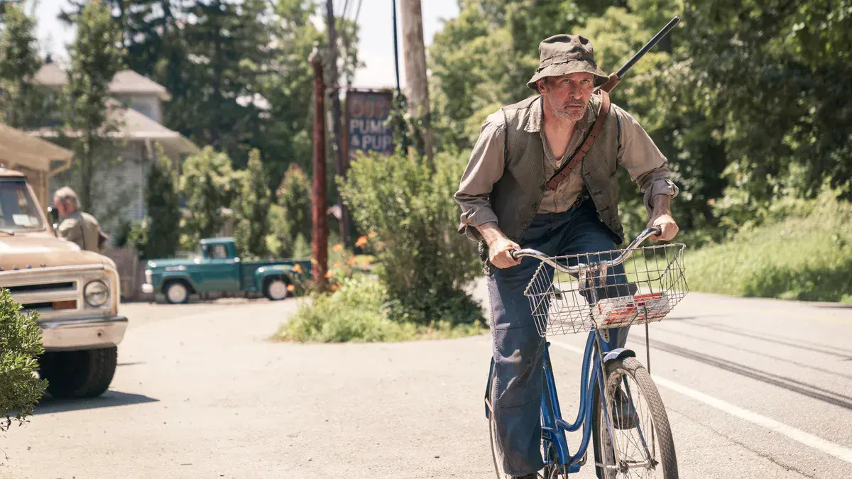 Nick Cordileone en Ralph, l'ermite de Crystal Lake, à vélo avec un fusil en bandoulière dans une rue de la ville, dans la série Crystal Lake