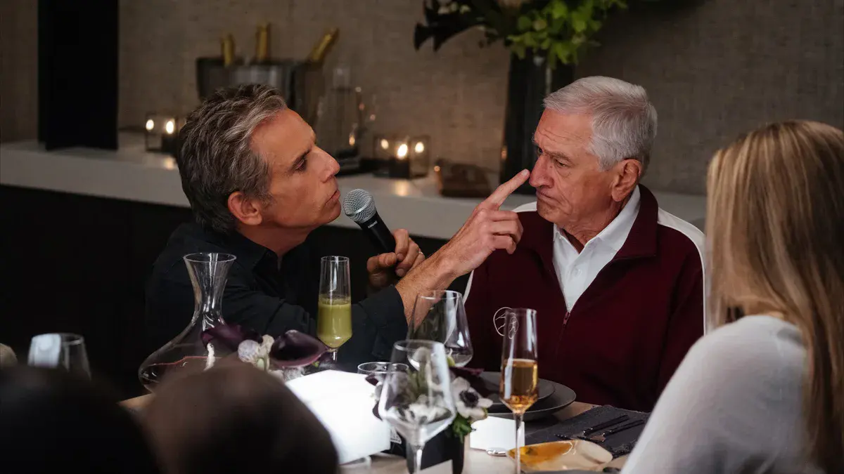 Ben Stiller, micro à la main, pointe le nez de Robert De Niro lors d'un dîner dans Mon beau-père, ma belle-fille et moi
