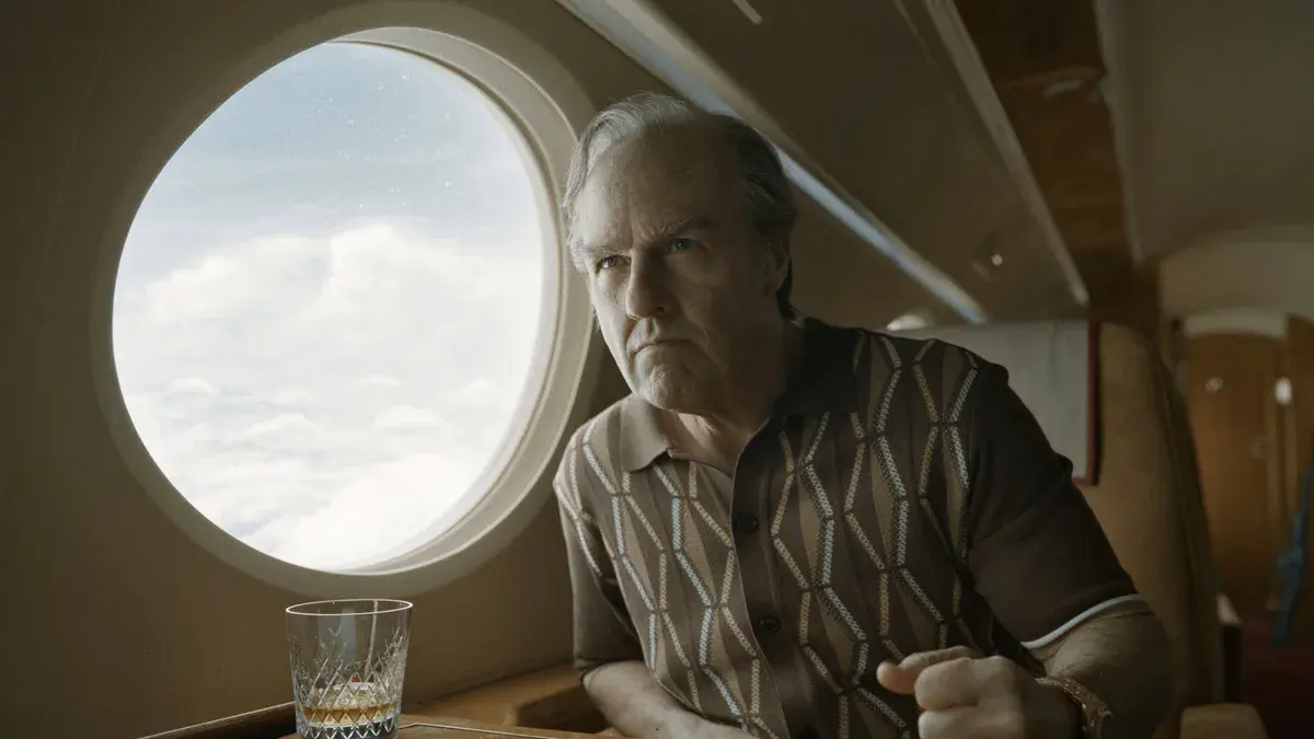Tom Cruise, chemise à motifs et verre de whisky, fixe le hublot d'un jet privé d'un air renfrogné dans Digger
