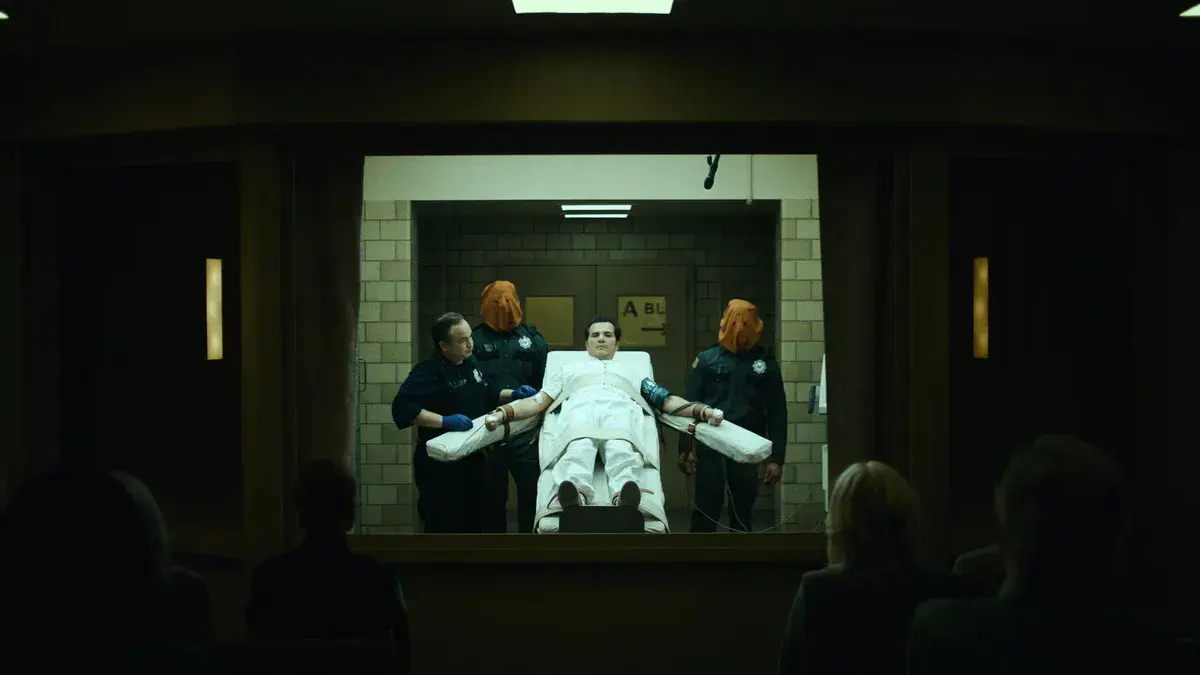 John Leguizamo, sanglé sur la table d'exécution entre deux gardiens à cagoule orange, derrière la vitre d'une salle où les témoins sont assis, dans The Exorcist: Martyrs