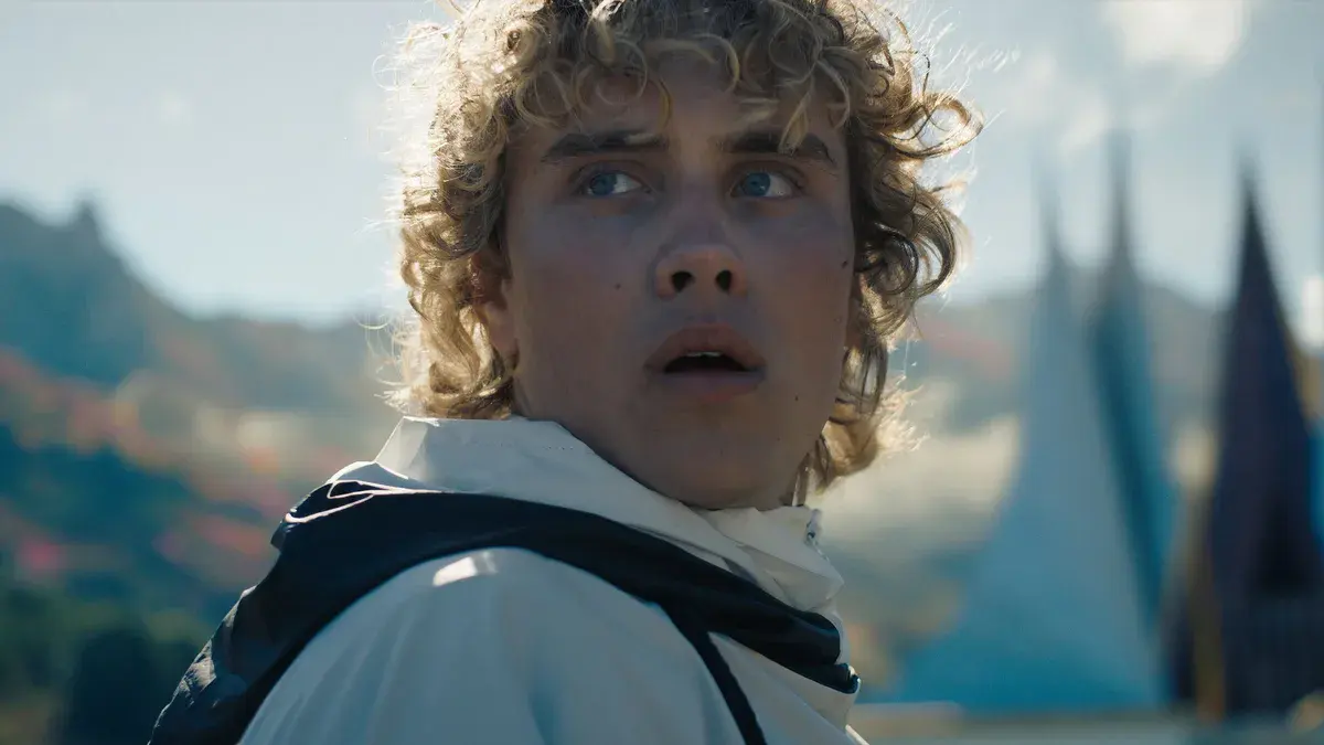 Joseph Zada en jeune Haymitch Abernathy, le regard levé, devant les tentes de l'arène dans Hunger Games : Lever de soleil sur la moisson