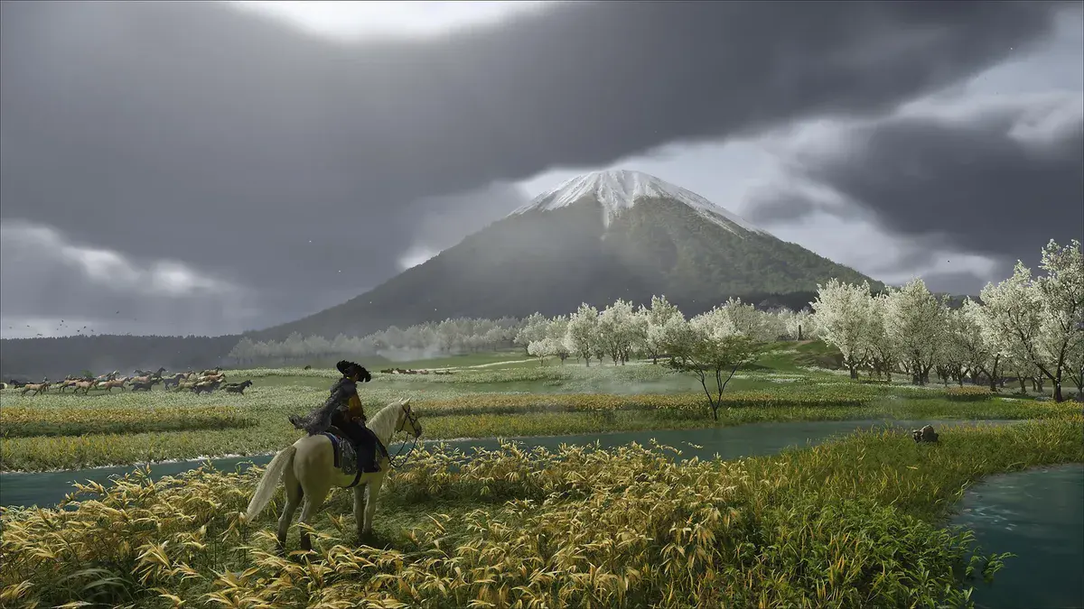 Atsu sur un cheval blanc au bord d'une rivière, face au mont Yōtei enneigé et à des chevaux sauvages, dans Ghost of Yōtei