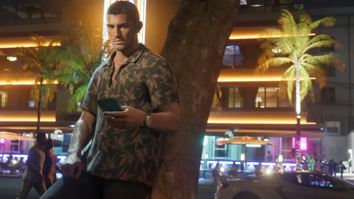 GTA 6 : Jason Duval, chemise à motifs de feuilles, adossé à un palmier de Vice City la nuit, téléphone en main devant des façades éclairées