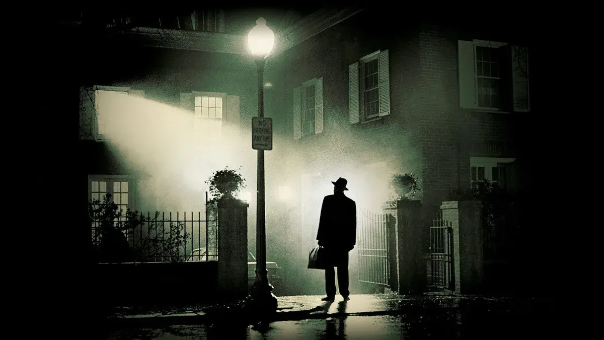 Le père Merrin, chapeau sur la tête et valise à la main, sous un réverbère devant la maison des MacNeil dans L'Exorciste de William Friedkin