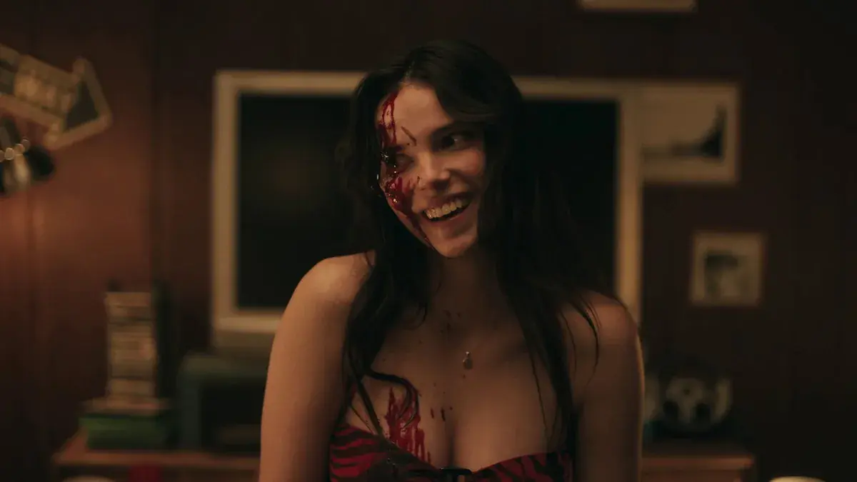 Inde Navarrette en Nikki, le visage en sang, sourit dans une chambre dans Obsession de Curry Barker