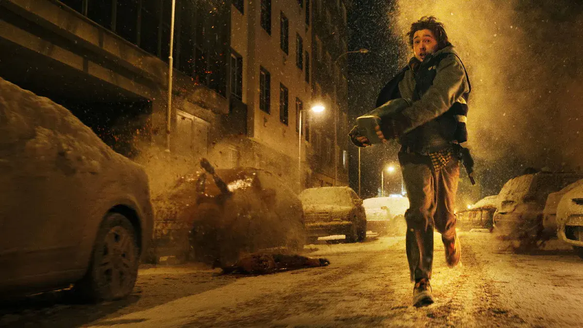 Austin Abrams en Bryan, coursier médical, court dans une rue enneigée de Raccoon City dans Resident Evil de Zach Cregger