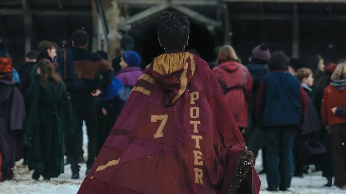 Harry, de dos dans la neige de Poudlard, porte une cape de Quidditch bordeaux marquée Potter et du numéro 7, dans la série Harry Potter de HBO