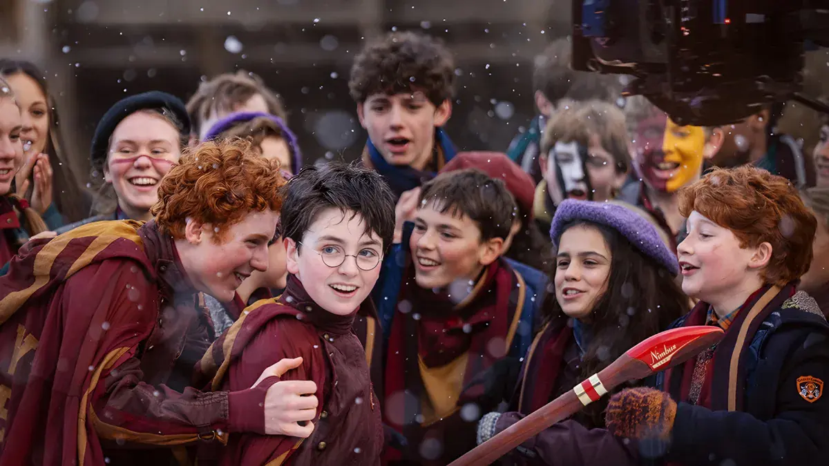 Harry entouré d'un jumeau Weasley, de Ron et d'élèves de Gryffondor en écharpes rouge et or sous la neige, dans la série Harry Potter de HBO