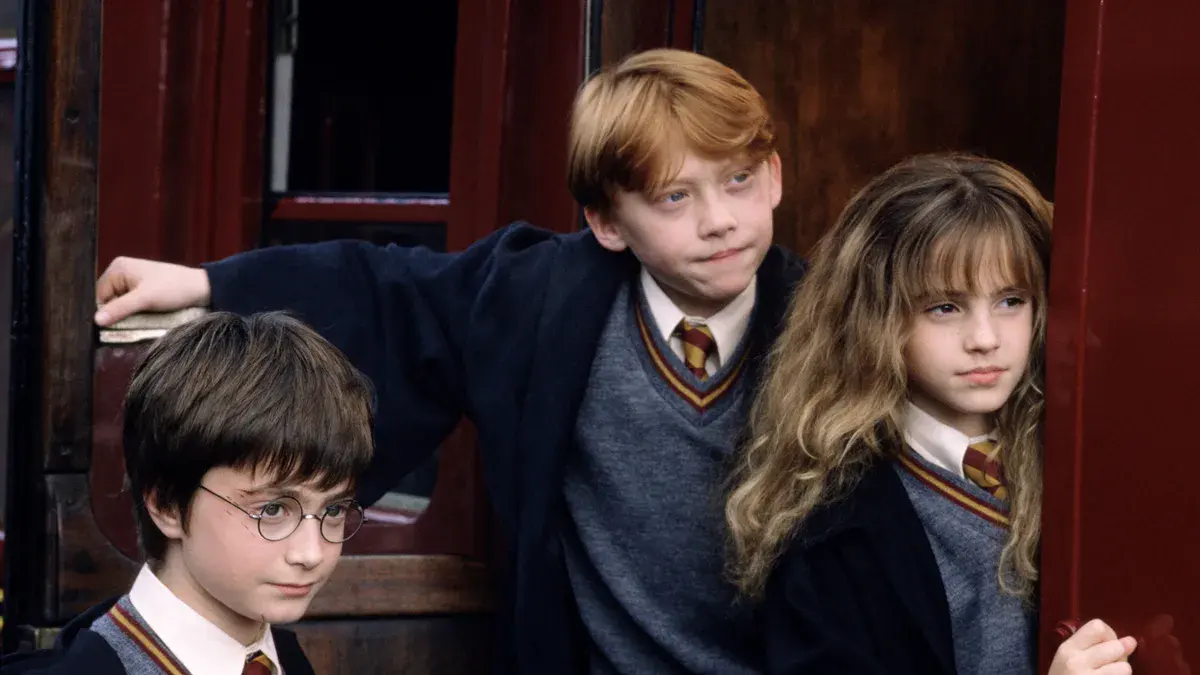 Harry, Ron et Hermione enfants en uniforme de Gryffondor à la porte d'un wagon du Poudlard Express dans Harry Potter à l'école des sorciers