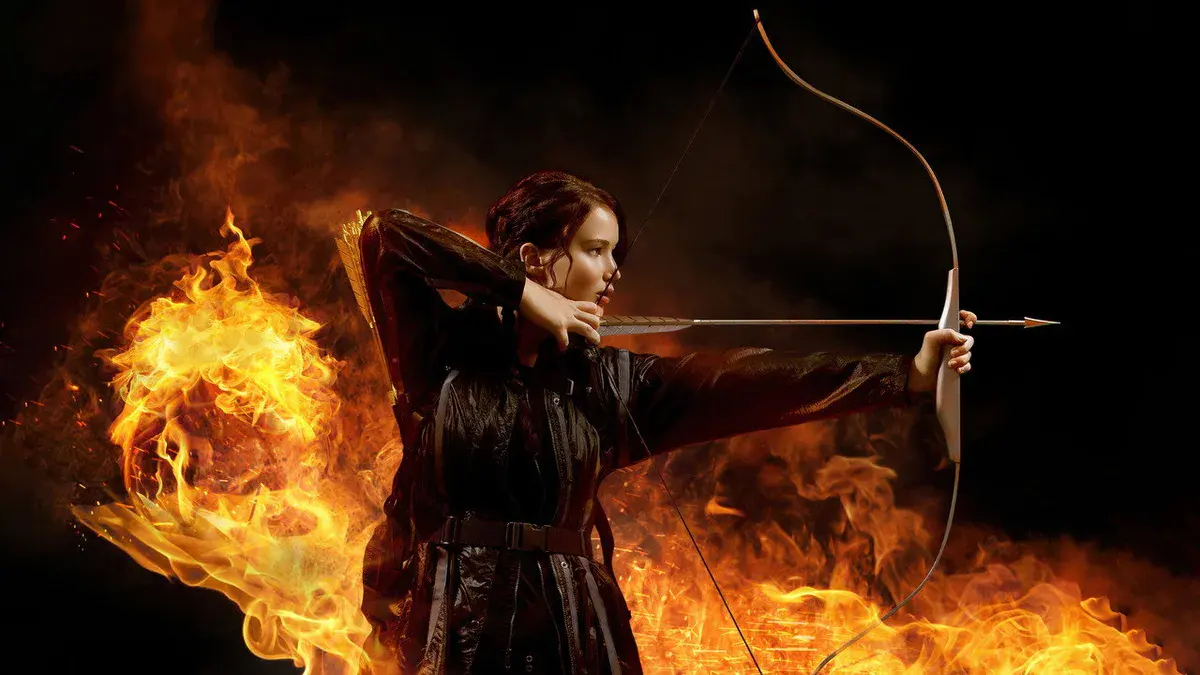 Jennifer Lawrence en Katniss Everdeen, arc bandé devant des flammes, sur un visuel promotionnel de Hunger Games (2012)