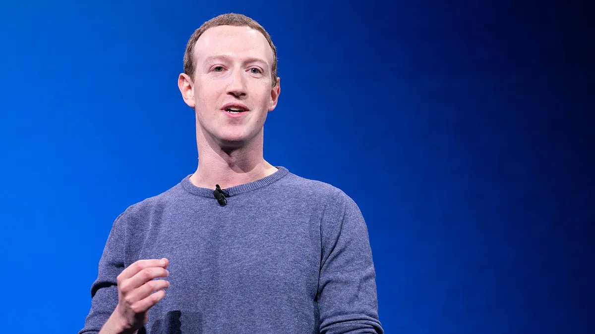 Mark Zuckerberg, patron de Meta, en pull bleu, parle sur la scène de la conférence F8 devant un fond bleu