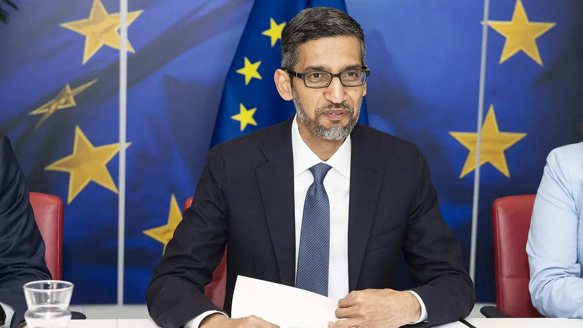 Sundar Pichai, patron de Google, en costume sombre devant des drapeaux européens lors d'une réunion à la Commission européenne