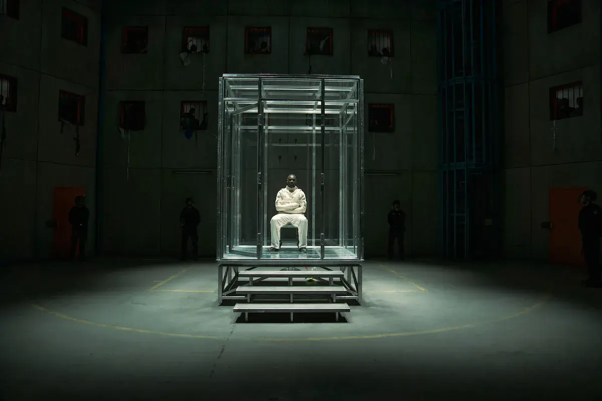 Omar Sy en Assane Diop, tenue blanche, seul dans une cellule de verre au milieu d'un hall de prison, dans Lupin partie 4