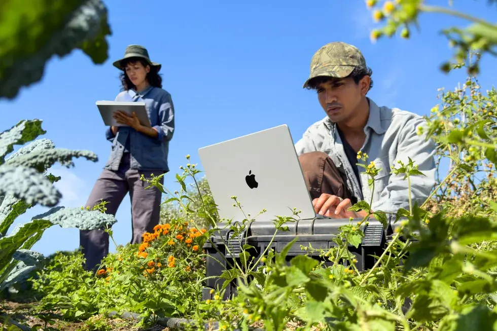 MacBook Pro 14 pouces M6 argent utilisé en extérieur, au milieu d'un potager, à côté d'une personne qui tient un iPad