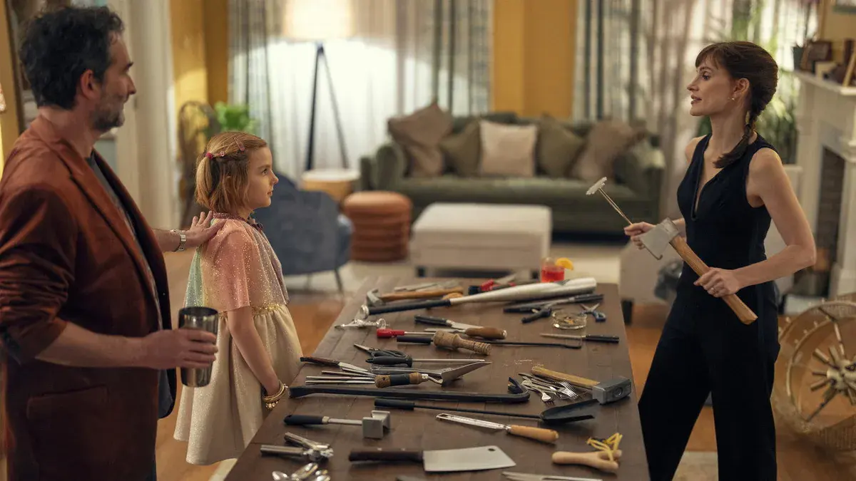 Jay Duplass, Arabella Olivia Clark et Jessica Chastain autour d'une table couverte d'outils dans le salon familial de Malfaisante