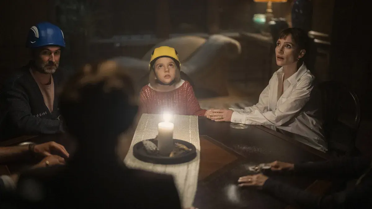 Bela, casque jaune sur la tête, tient la main d'Ursula (Jessica Chastain) autour d'une bougie pendant une séance de spiritisme dans Malfaisante