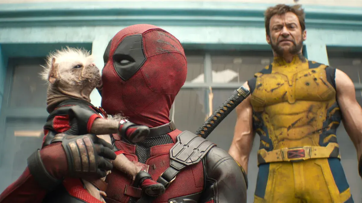 Deadpool, joué par Ryan Reynolds, tient le chien Dogpool dans ses bras à côté de Wolverine, joué par Hugh Jackman, dans Deadpool & Wolverine