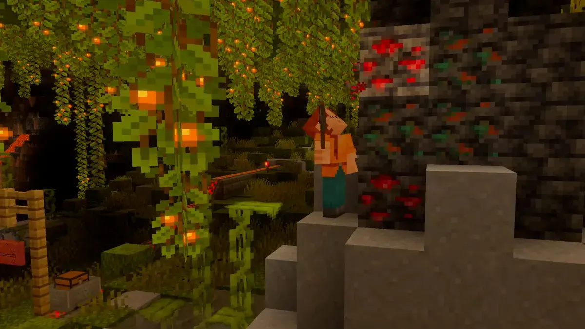 Un personnage aux cheveux roux lève un outil devant un bloc de minerai de redstone, de nuit, sous des lianes chargées de baies lumineuses, dans Minecraft sur Switch 2