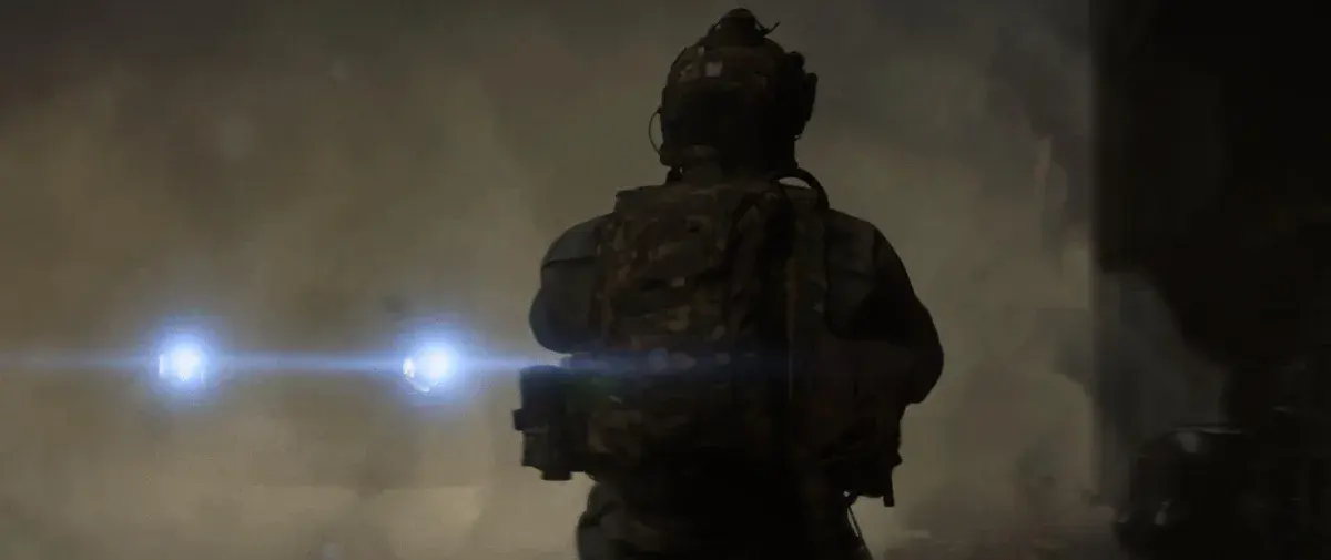 Un soldat vu de dos, casque et sac sur les épaules, avance à contre-jour vers deux lampes perçant la fumée dans Call of Duty: Modern Warfare 4