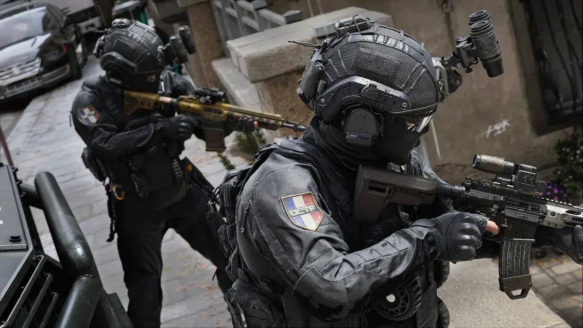 Deux membres des forces spéciales en noir, écusson tricolore à l'épaule, progressent fusil épaulé dans une rue de Modern Warfare 4