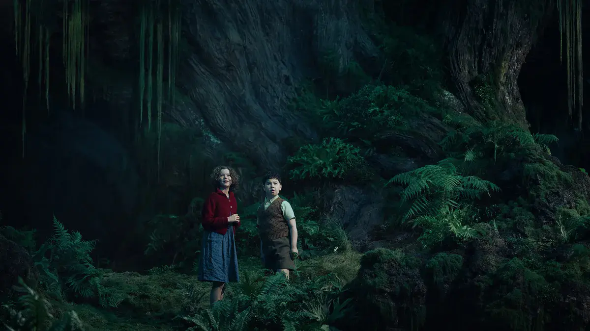 Polly et Digory, joués par Beatrice Campbell et David McKenna, dans une forêt moussue de Narnia : Le Neveu du magicien