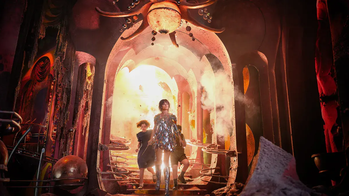 Emma Mackey en Jadis, robe à sequins, sort d'un passage illuminé avec Polly et Digory dans Narnia : Le Neveu du magicien