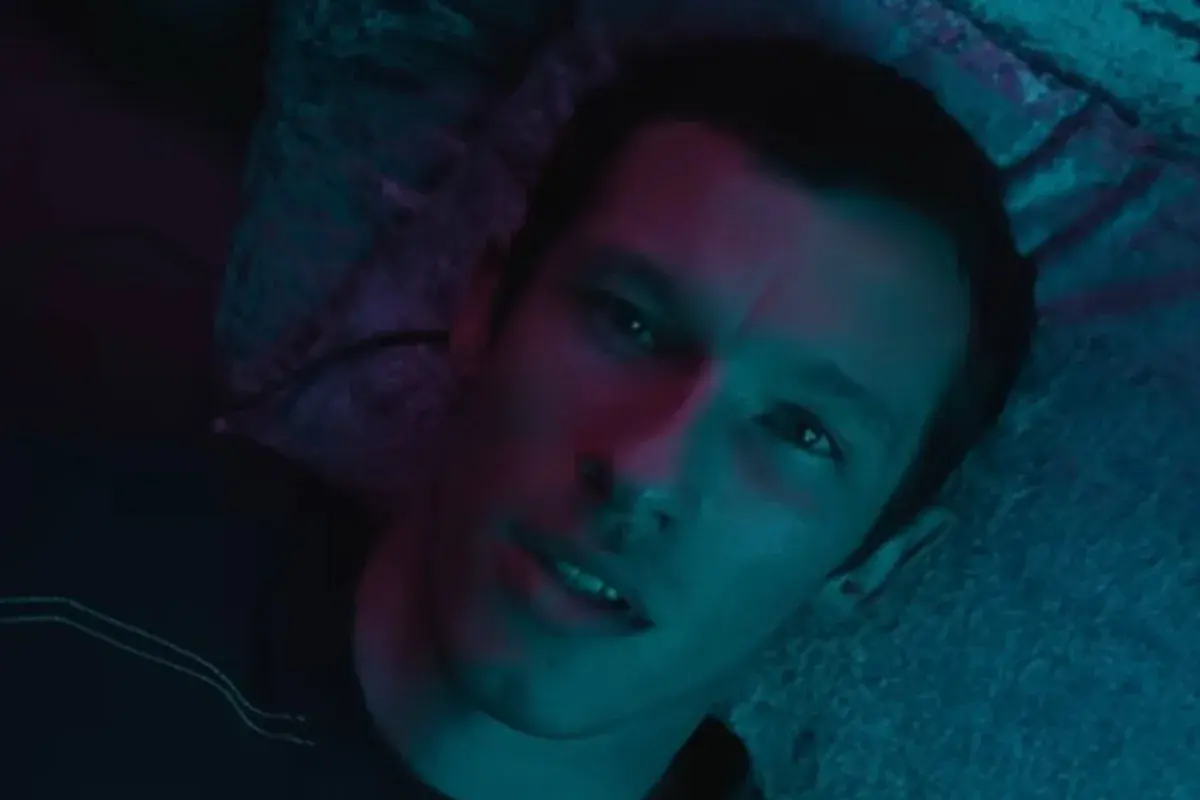 Gros plan sur Callum Turner, allongé sous une lumière bleue et rouge, dans la bande-annonce de Neuromancien