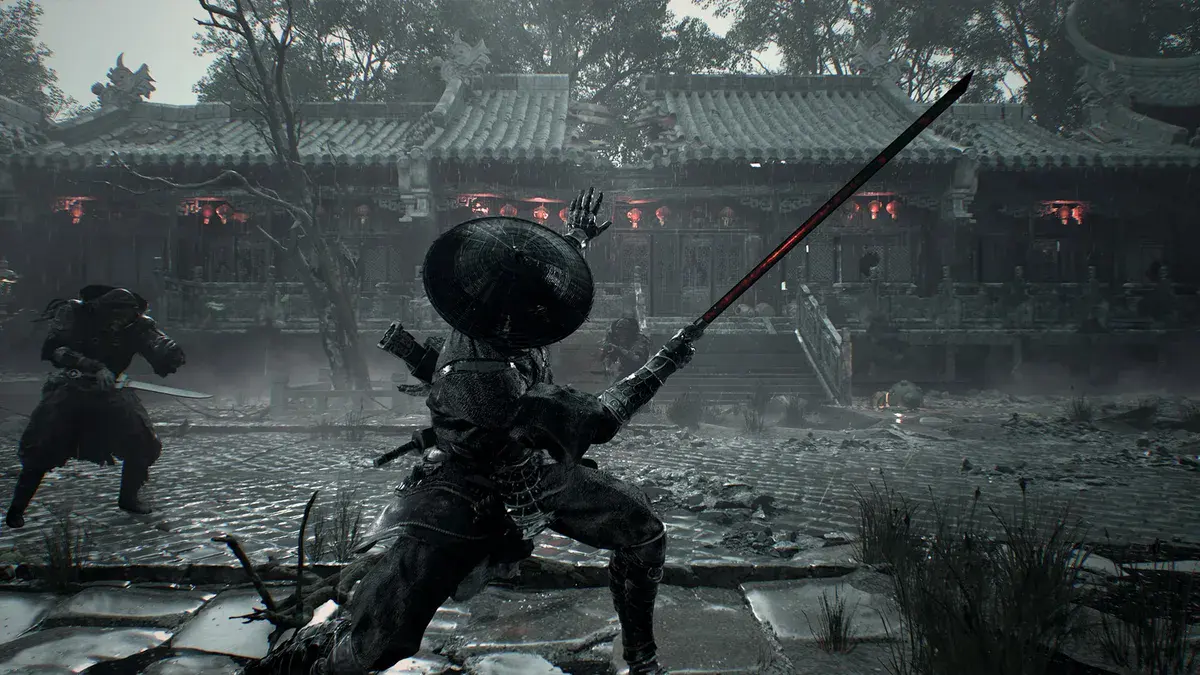Un épéiste coiffé d'un chapeau de paille se met en garde, lame levée, face à un ennemi dans la cour pavée d'un temple dans Phantom Blade Zero