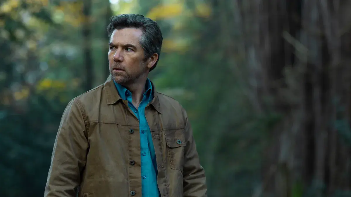 Patrick Brammall en Ian Ridley, veste de toile sur le dos, au milieu d'une forêt, dans Portée disparue