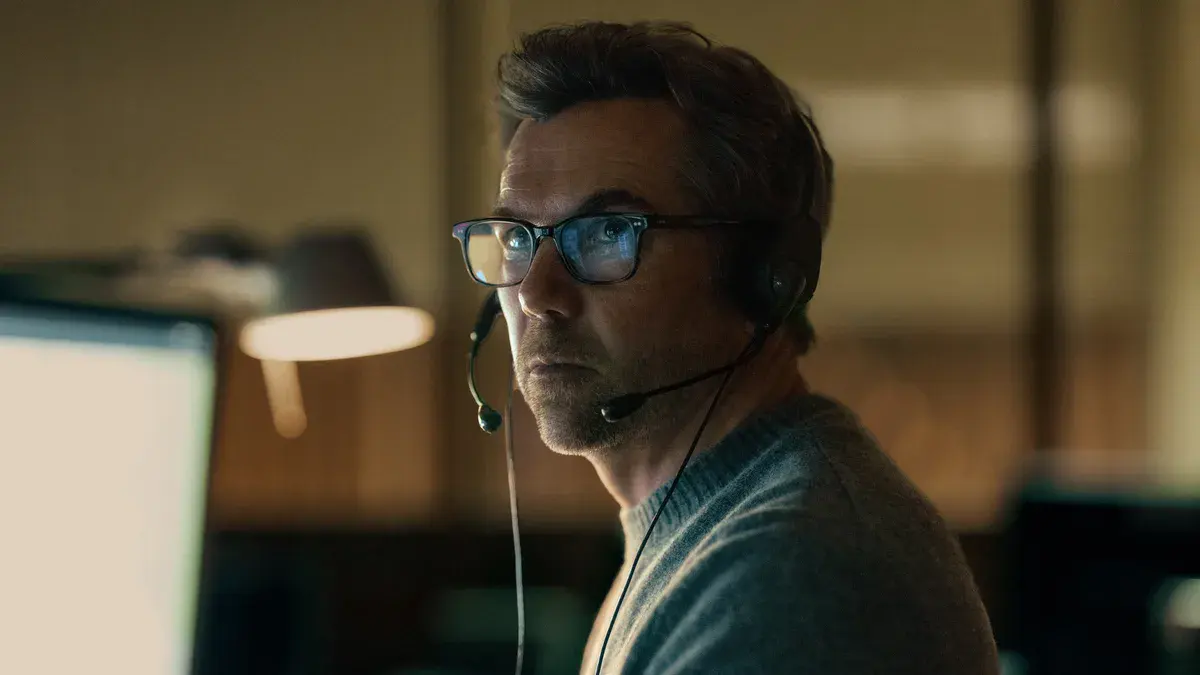 Patrick Brammall en Ian Ridley, casque et lunettes, au standard des appels d'urgence dans Portée disparue sur Apple TV