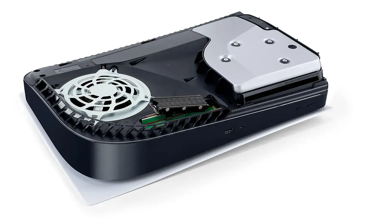 Une PS5 couchée, capot retiré, laisse voir son emplacement d'extension où est installé un SSD M.2 équipé d'un dissipateur, à côté du ventilateur