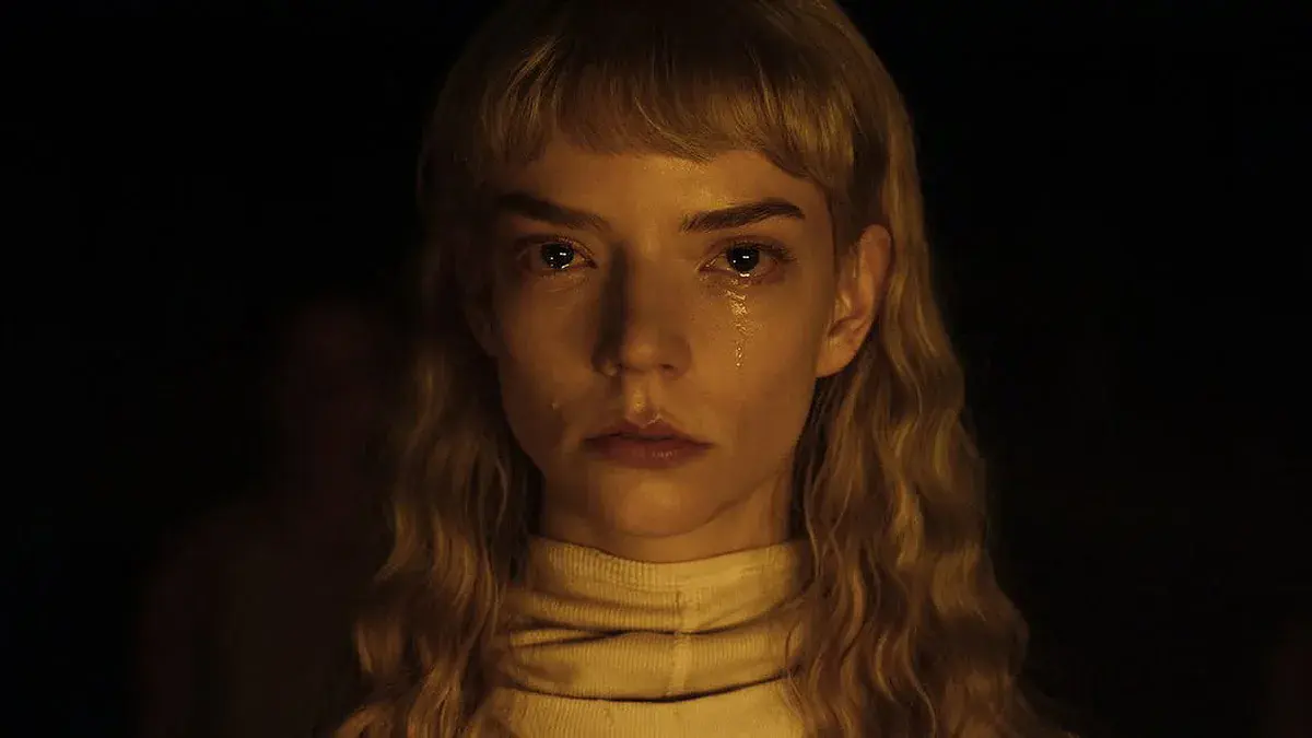Gros plan d'Anya Taylor-Joy en larmes, cheveux blonds ondulés et col roulé crème, sur fond noir, dans le film Sacrifice de Romain Gavras