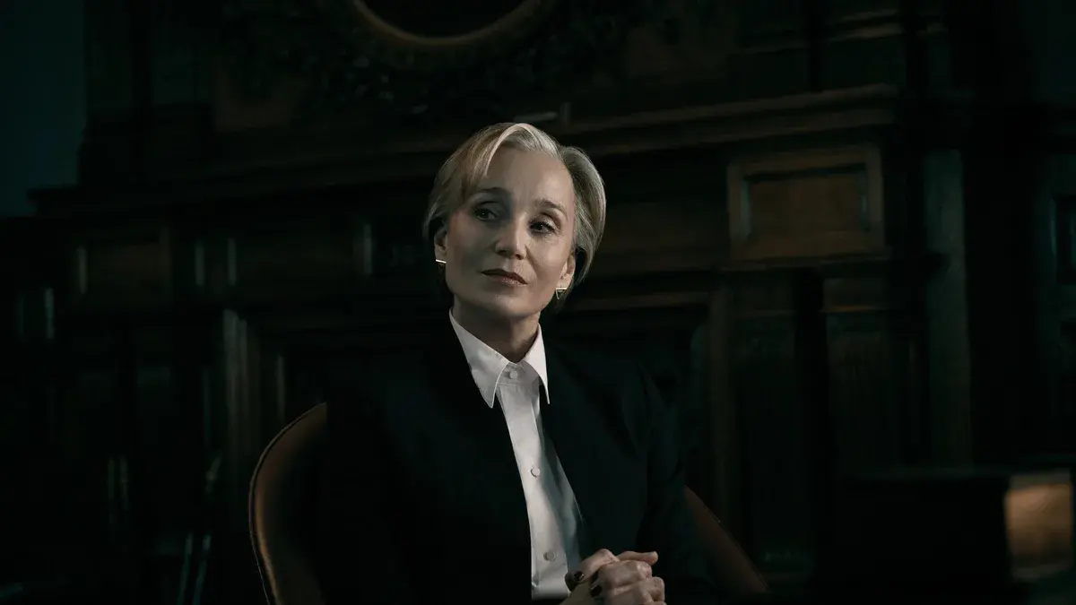 Kristin Scott Thomas en Diana Taverner, tailleur noir et chemise blanche, assise dans un bureau aux boiseries sombres dans la saison 6 de Slow Horses