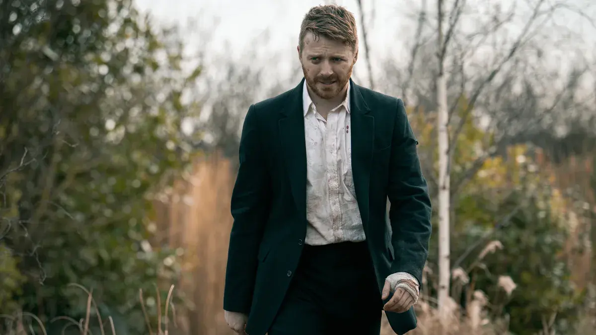 Jack Lowden en River Cartwright, chemise tachée de sang et main bandée, marche dans les herbes hautes dans la saison 6 de Slow Horses
