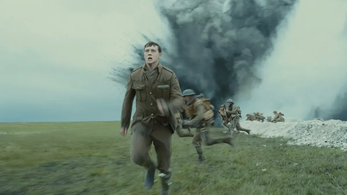 1917 : George MacKay court à travers un champ devant une explosion, au milieu des soldats britanniques montant à l'assaut