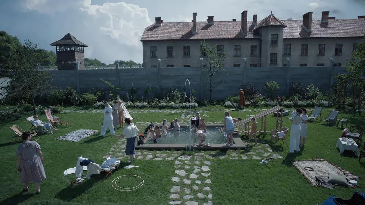 La Zone d'intérêt : la famille Höss et ses invités autour de la piscine du jardin, avec le mur et un mirador d'Auschwitz en arrière-plan