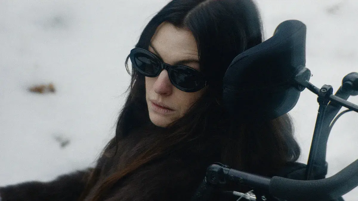 Anne Hathaway, lunettes noires et manteau de fourrure, dans un fauteuil roulant au milieu de la neige dans Verity