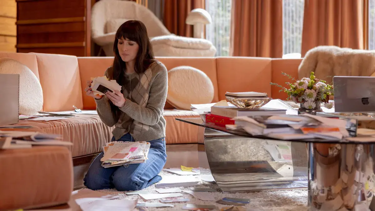 Dakota Johnson, à genoux sur un tapis, trie des lettres et des feuillets dans le salon des Crawford dans Verity