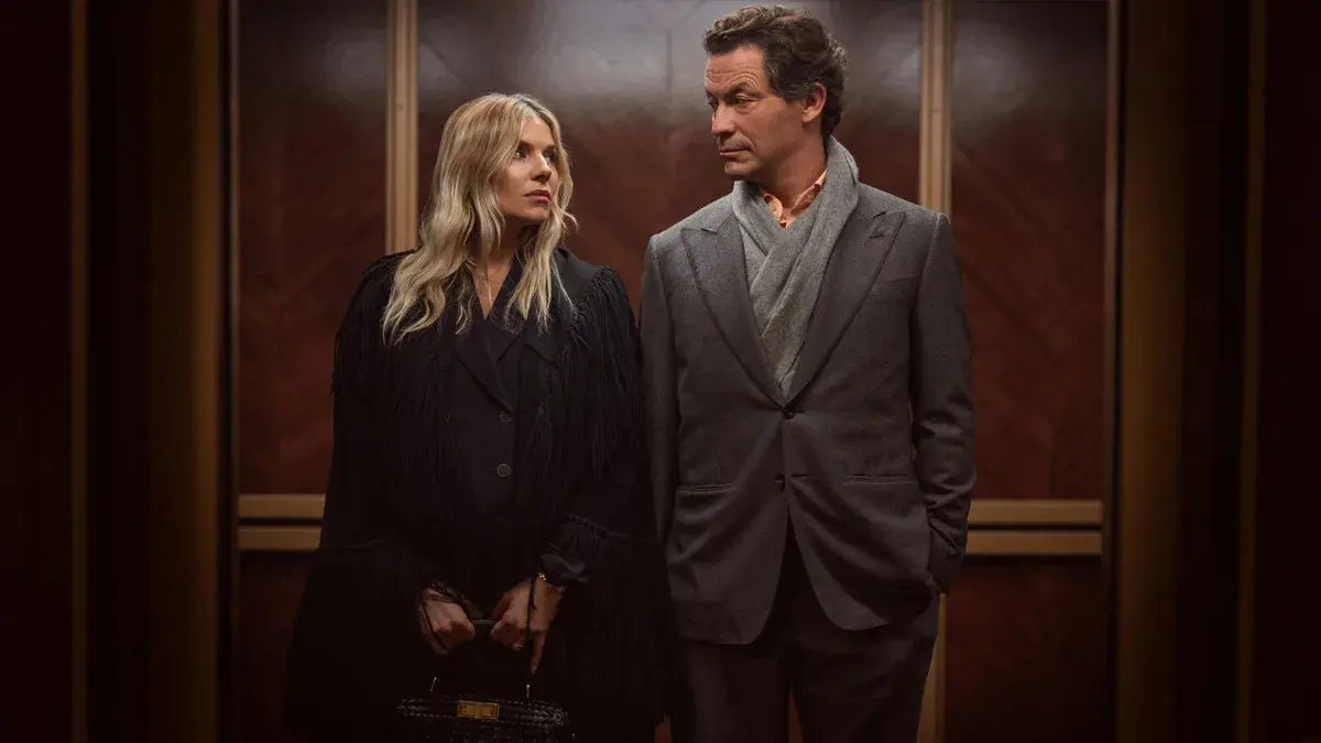 Sienna Miller et Dominic West côte à côte dans un ascenseur aux boiseries sombres, dans la série War de George Kay