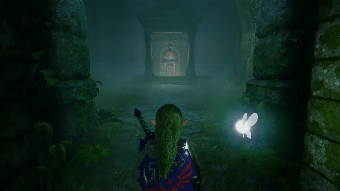Link adulte, de dos avec l'épée de Légende et le bouclier d'Hylia, avance vers l'entrée du Temple de la Forêt dans la brume, Navi à ses côtés, dans le remake de Zelda: Ocarina of Time