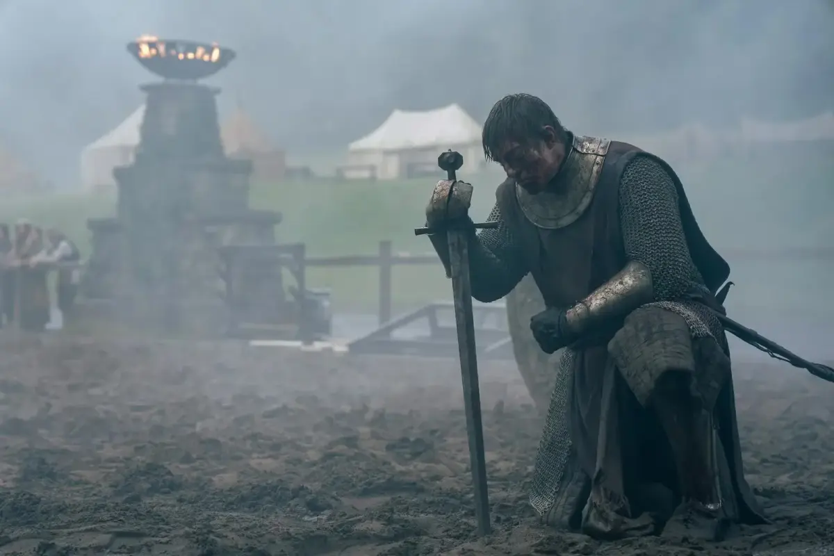 Dunk, en cotte de mailles couverte de boue, à genoux sur le champ du tournoi, appuyé sur son épée plantée dans le sol dans A Knight of the Seven Kingdoms