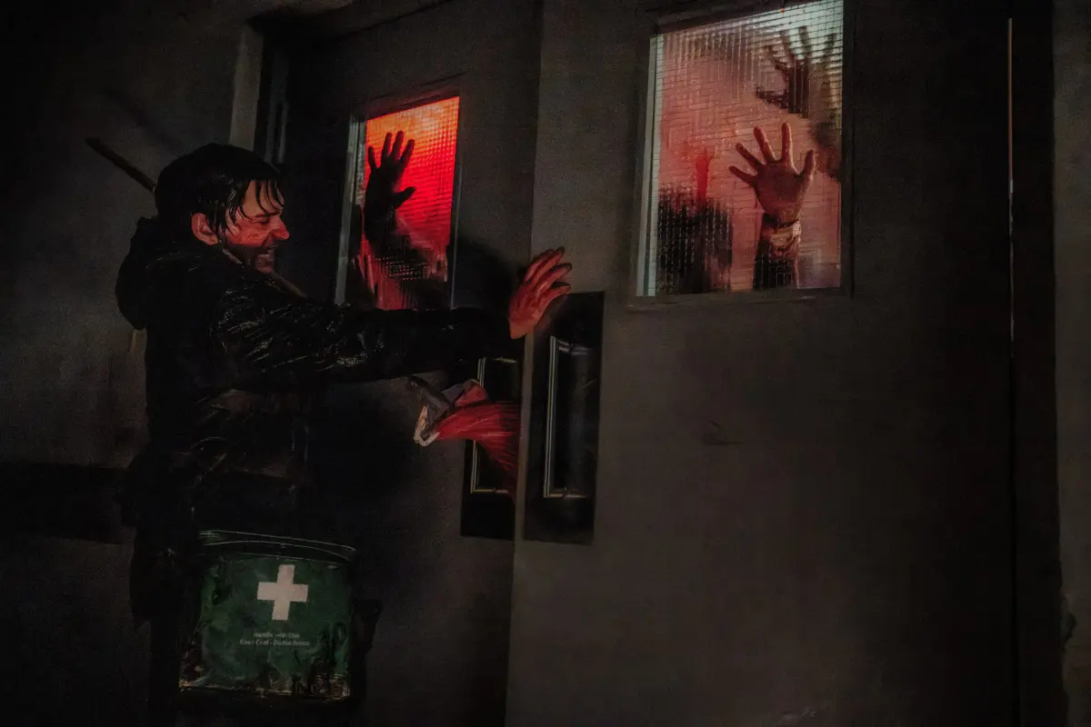 Un survivant trempé et ensanglanté retient une porte aux vitres éclairées de rouge, derrière lesquelles se pressent des mains d'infectés, dans Resident Evil de Zach Cregger